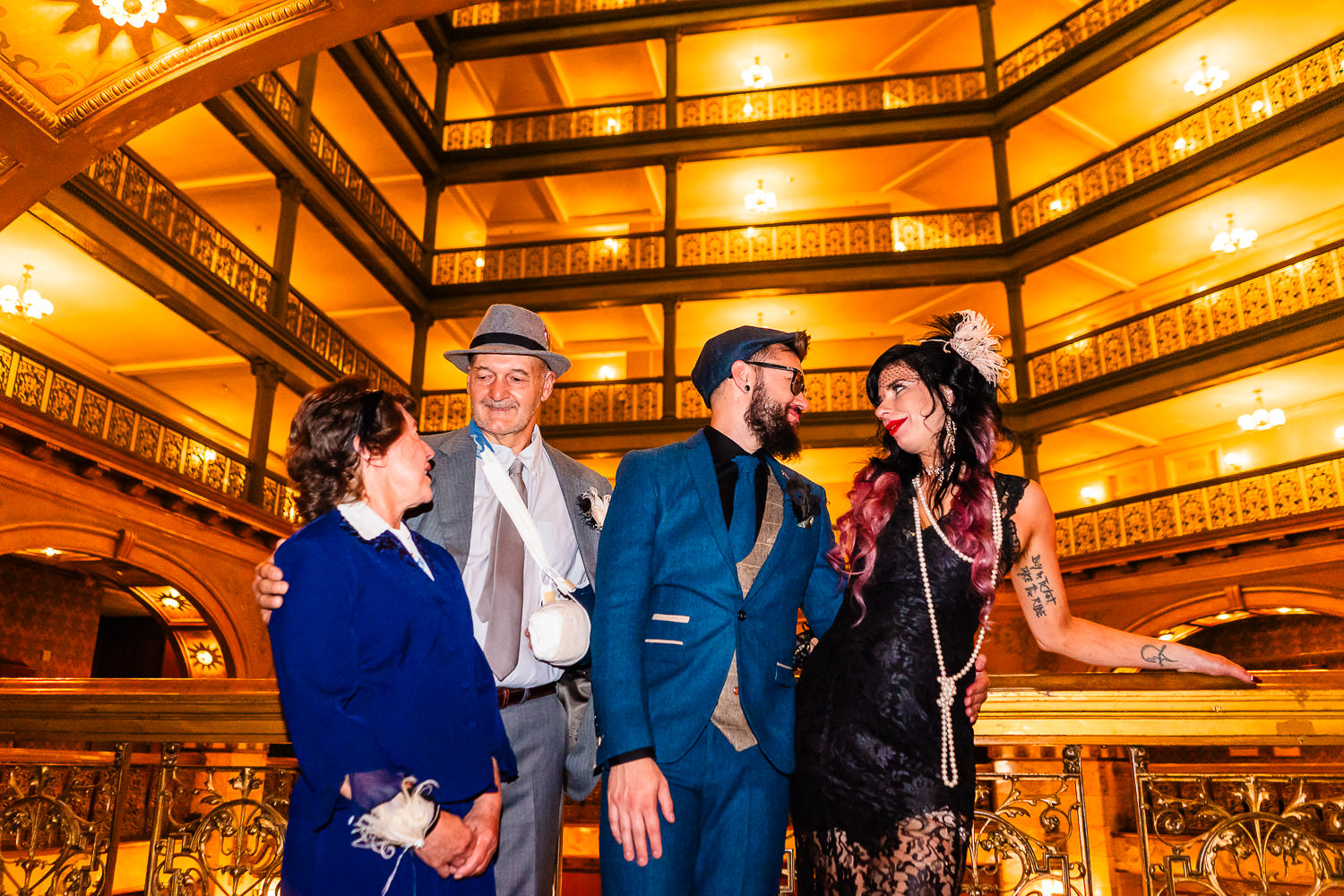 Four people dressed in vintage-inspired 1920s attire posing together in an elegant atrium during a Brown Palace wedding.