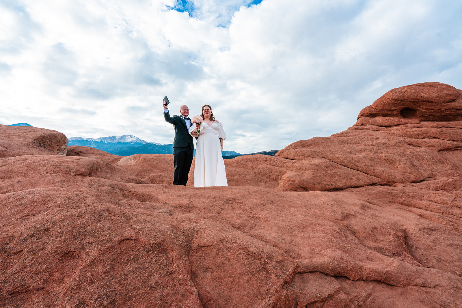 A bride and groom celebrate their marriage and raise their hands beneath a cloudy sky during their Garden of the Gods elopement at the High Point ceremony location.