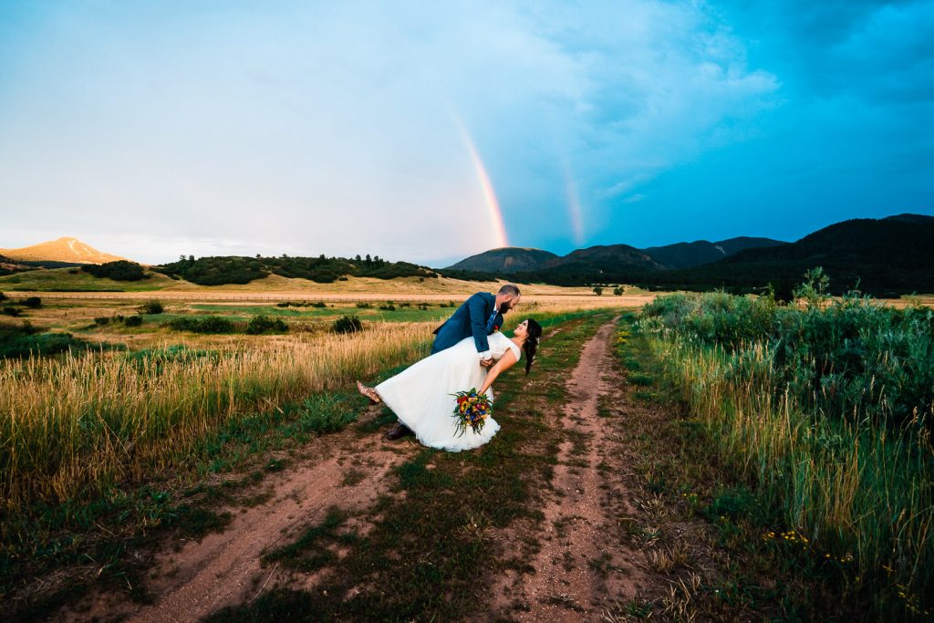 groom holds his bride beneath a double rainbow during a Colorado elopement