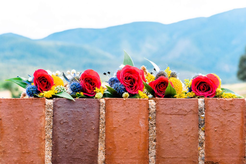 5 colorful boutonnieres rest beneath the mountains on a brick wall 
