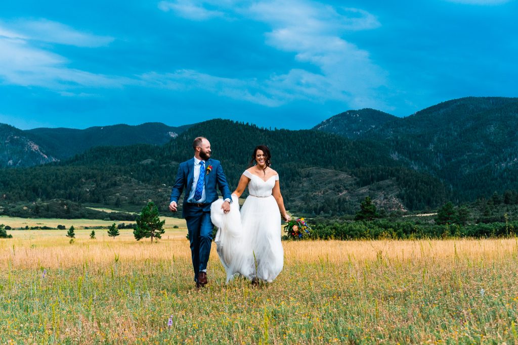newlyweds run through a field beneath the mountains during their Colorado elopement