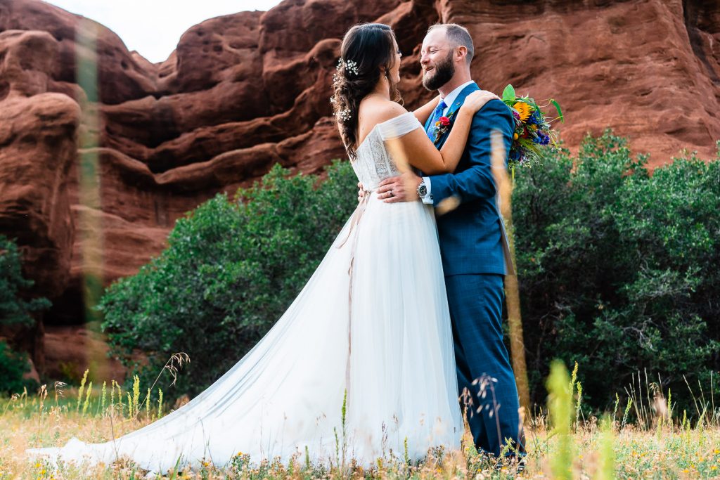 newlyweds hold each other beneath large red rock formations in Larkspur, Colorado
