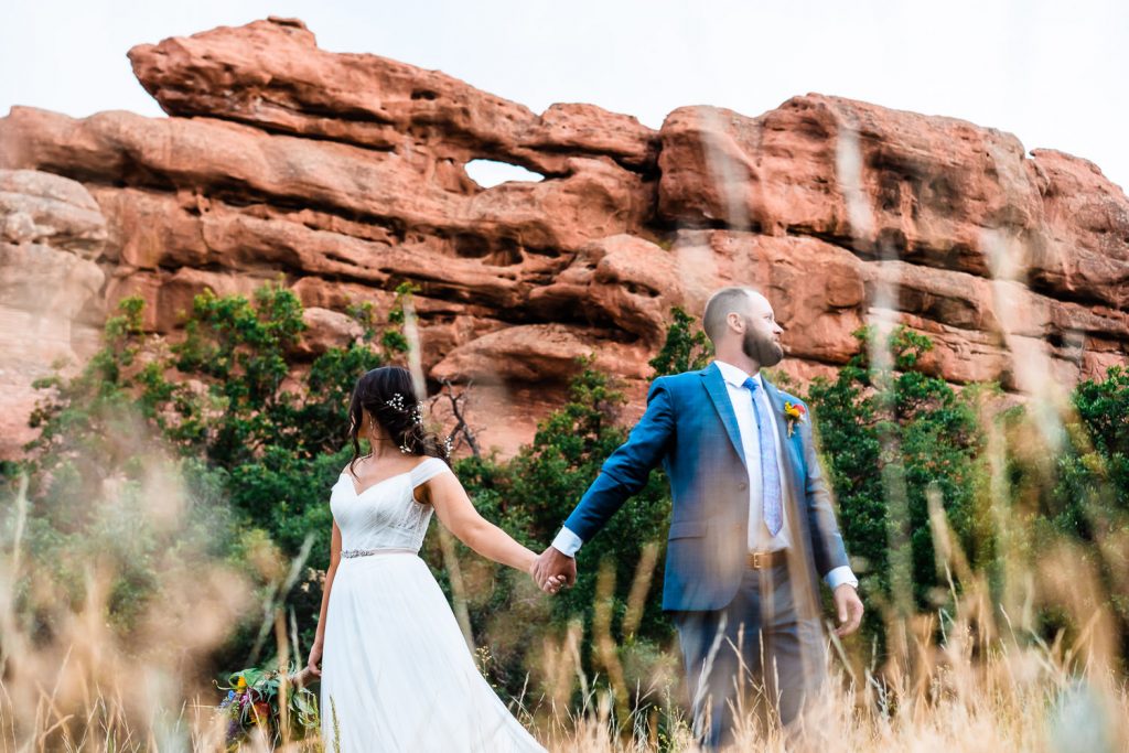 newlyweds hold hands beneath red rock formations during their Larkspur, Colorado elopement