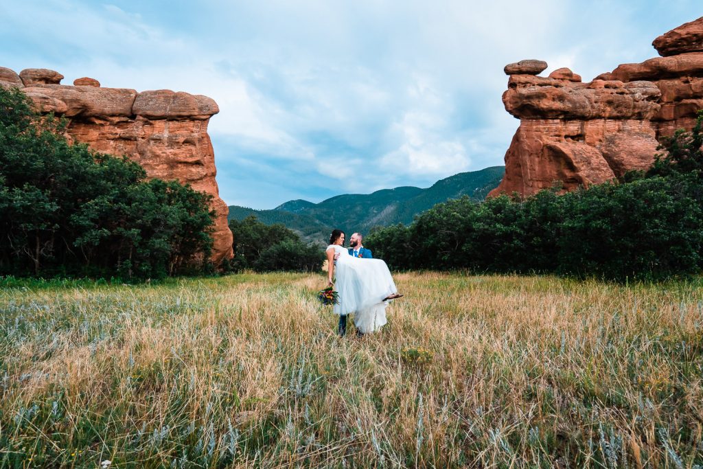 groom carries his bride beneath towering red rock formations during their Colorado elopement