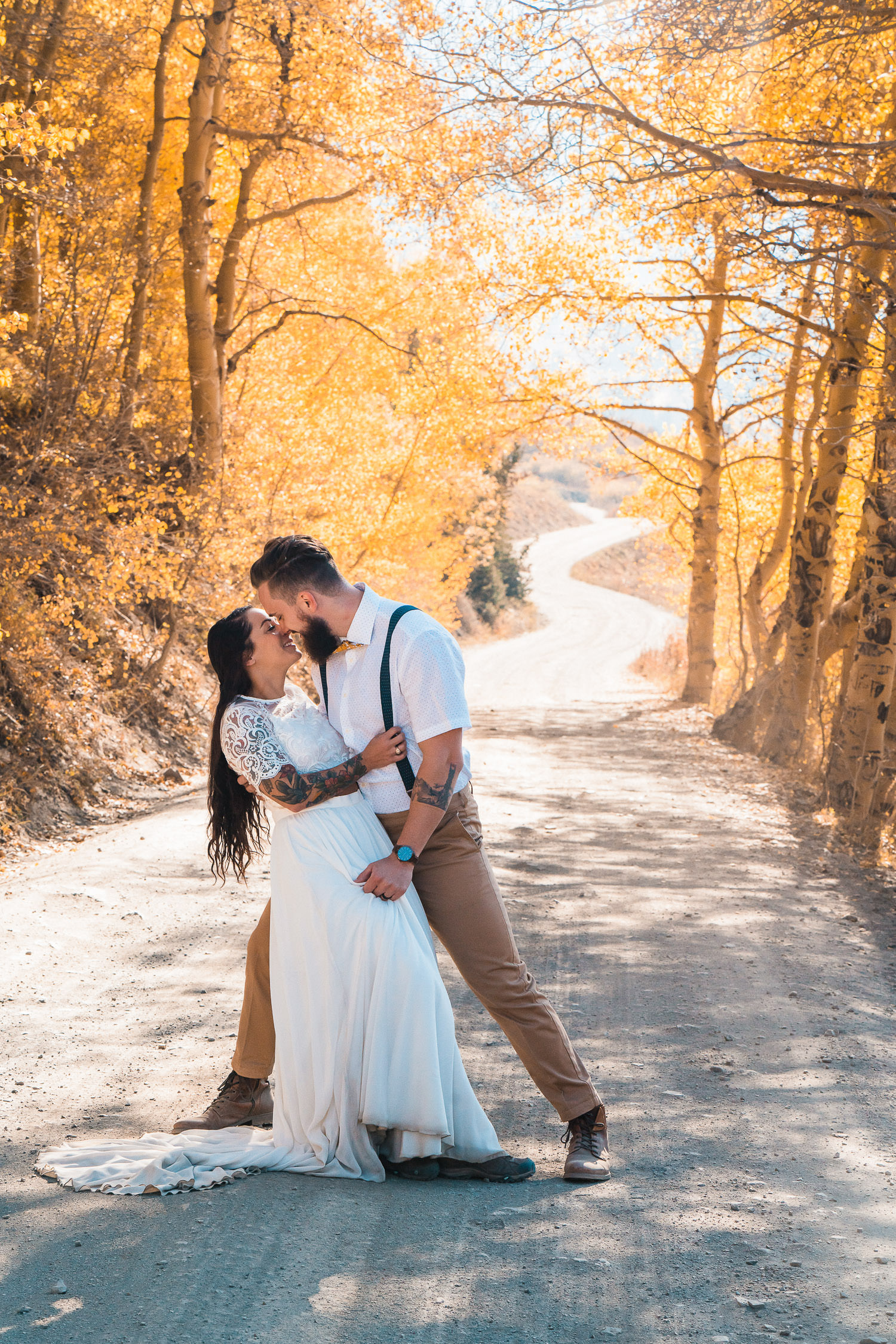 A bride and groom kiss while standing in a road surrounded by golden trees