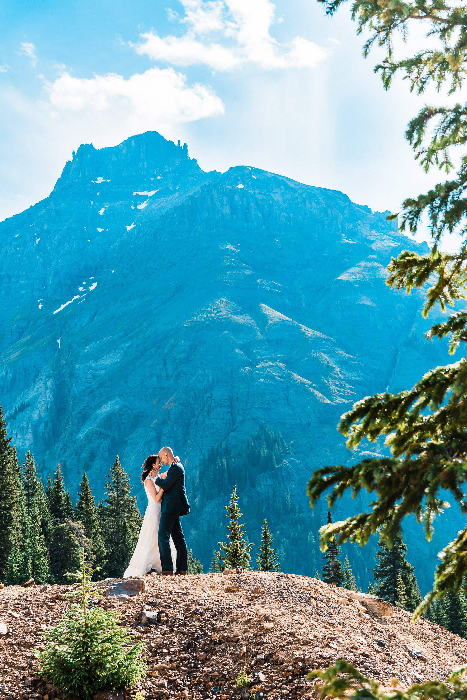A bride and groom pose on a mountain top in Colorado