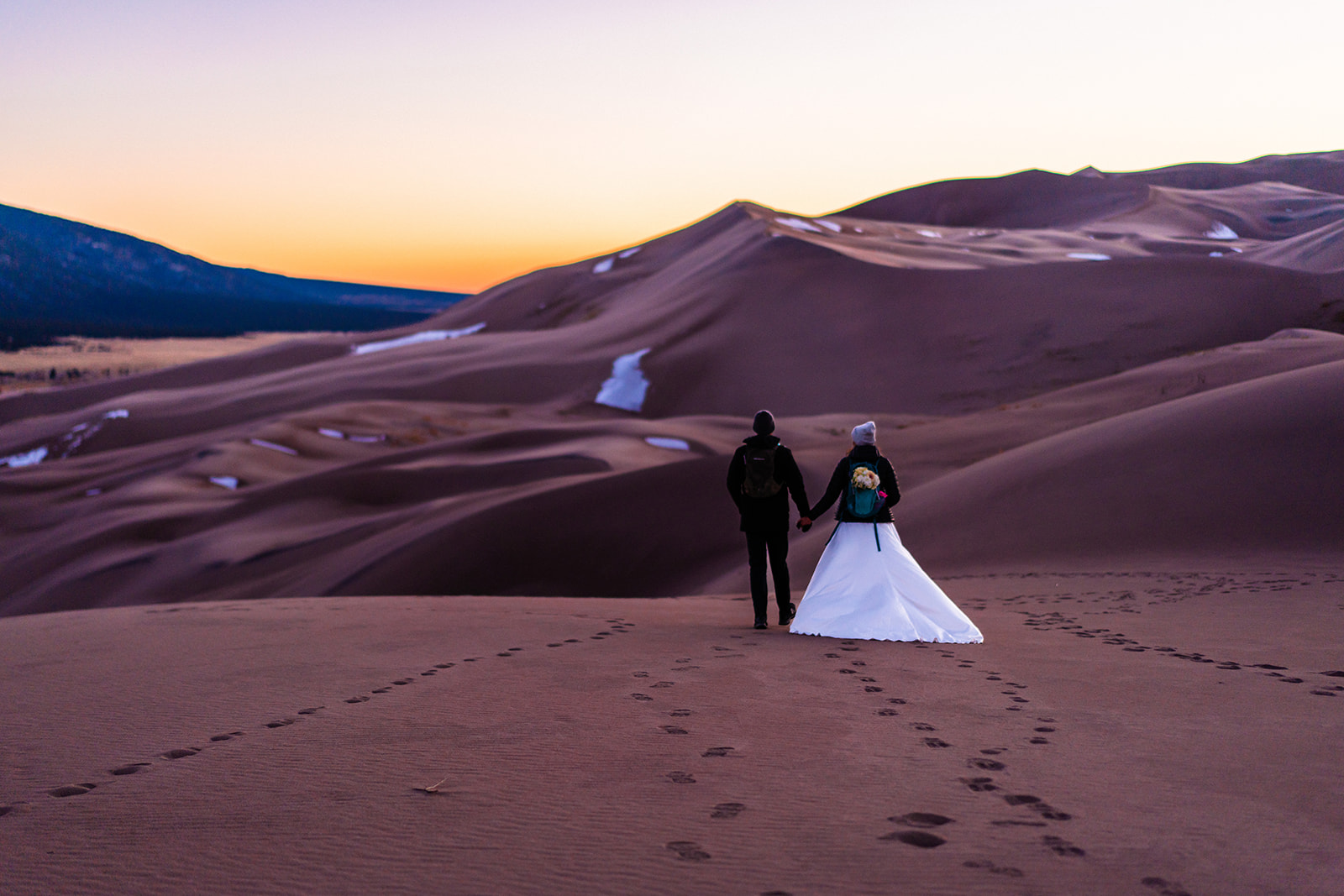 A bride and groom walking through the sand dunes during their elopement at sunset at one of the best places to elope in Colorado.