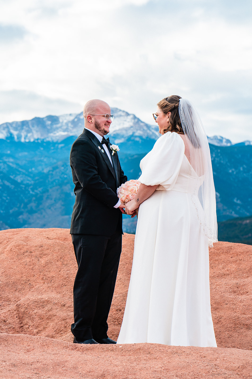 A bride and groom standing on top of a red rock in one of the best places to elope in Colorado during their Garden of the Gods elopement.