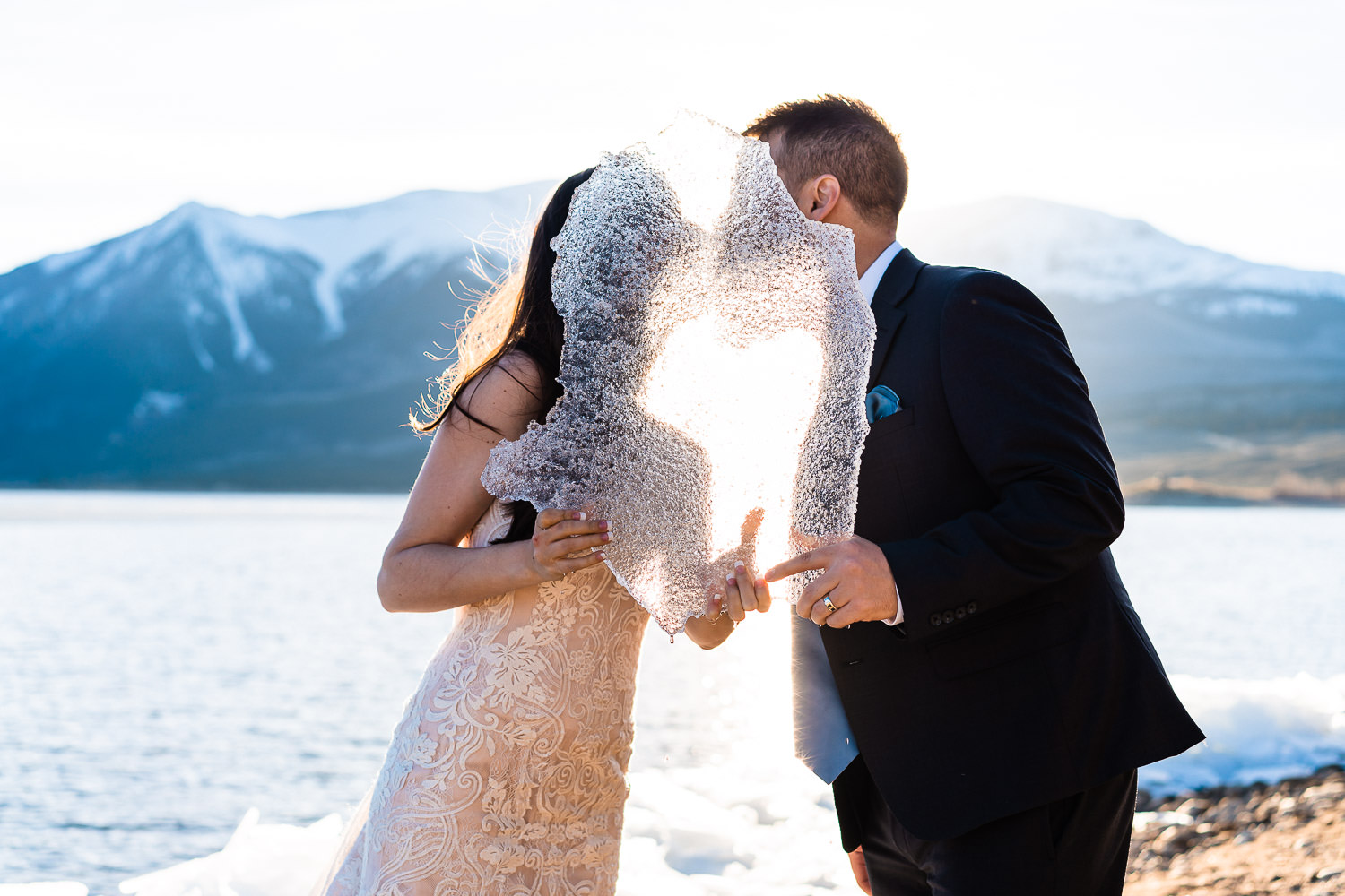 A couple eloping behind a piece of frozen lake water
