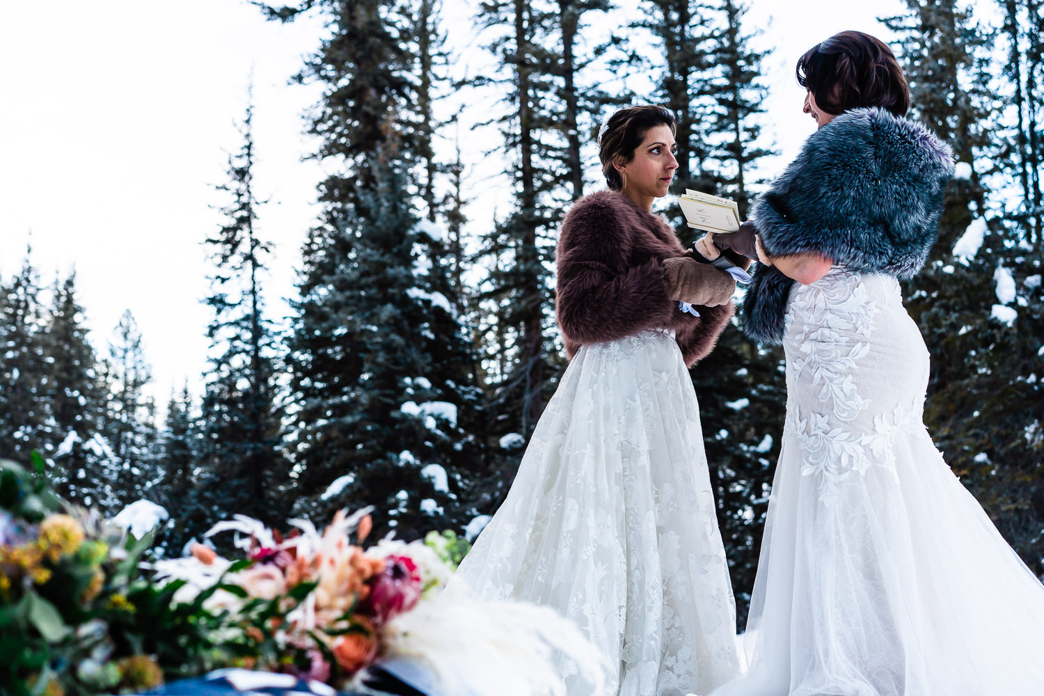 Lesbians getting married by a snowy riverbank during their LGBTQ+ elopement ceremony in Colorado