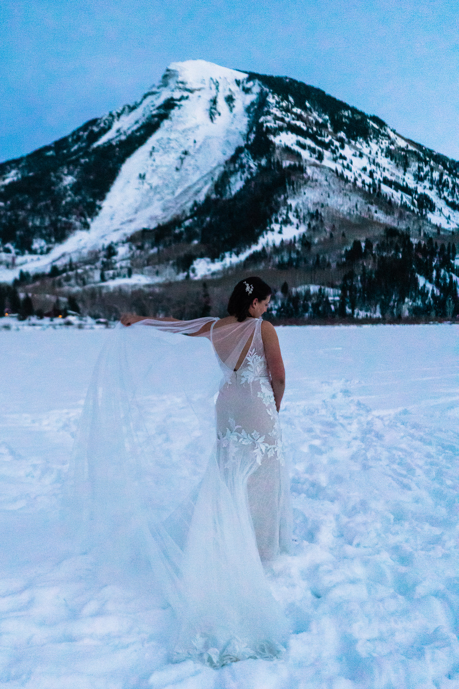 newlywed bride holding her veil in a snowy field