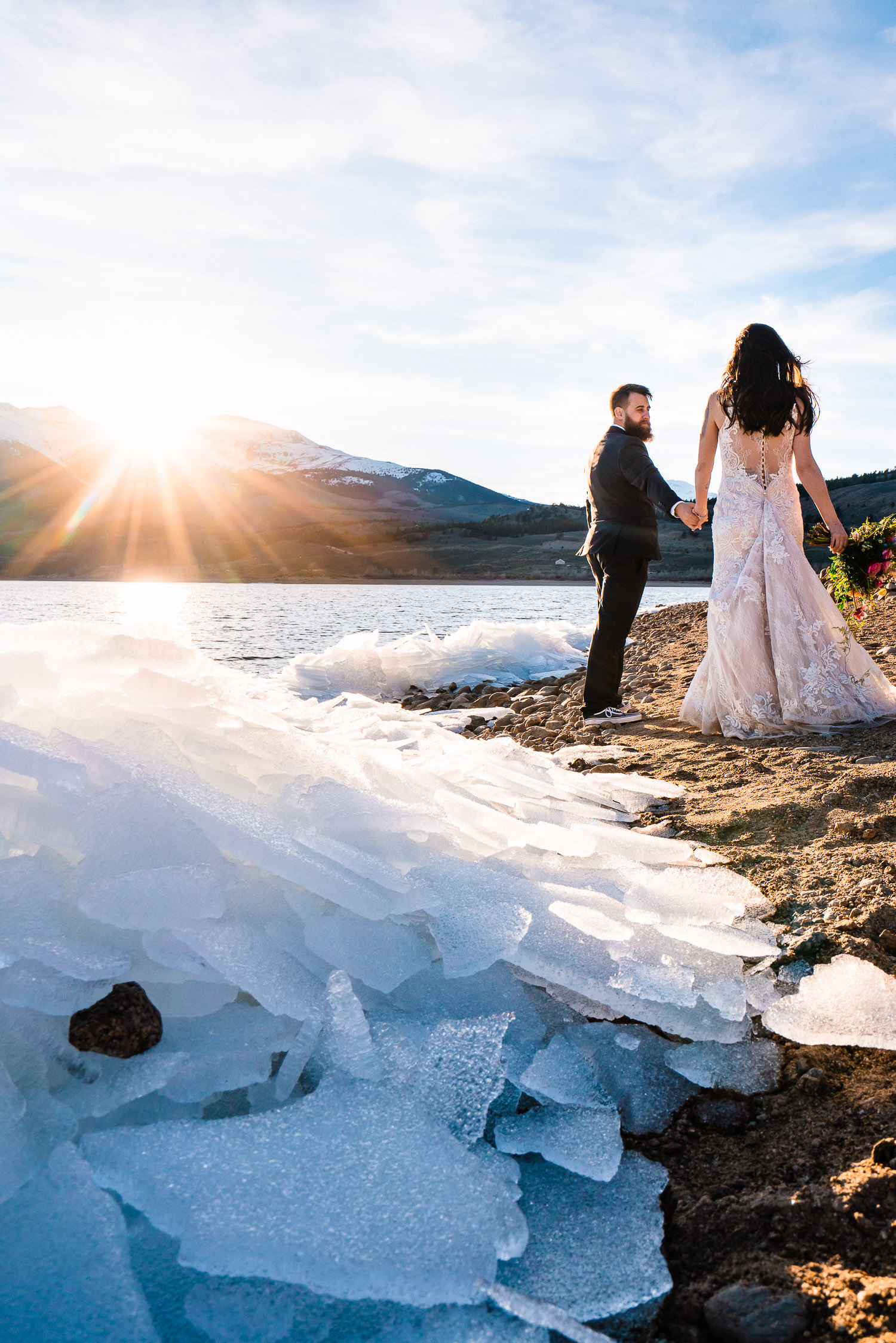 newlyweds explore frozen sheets of ice on a lake's shoreline