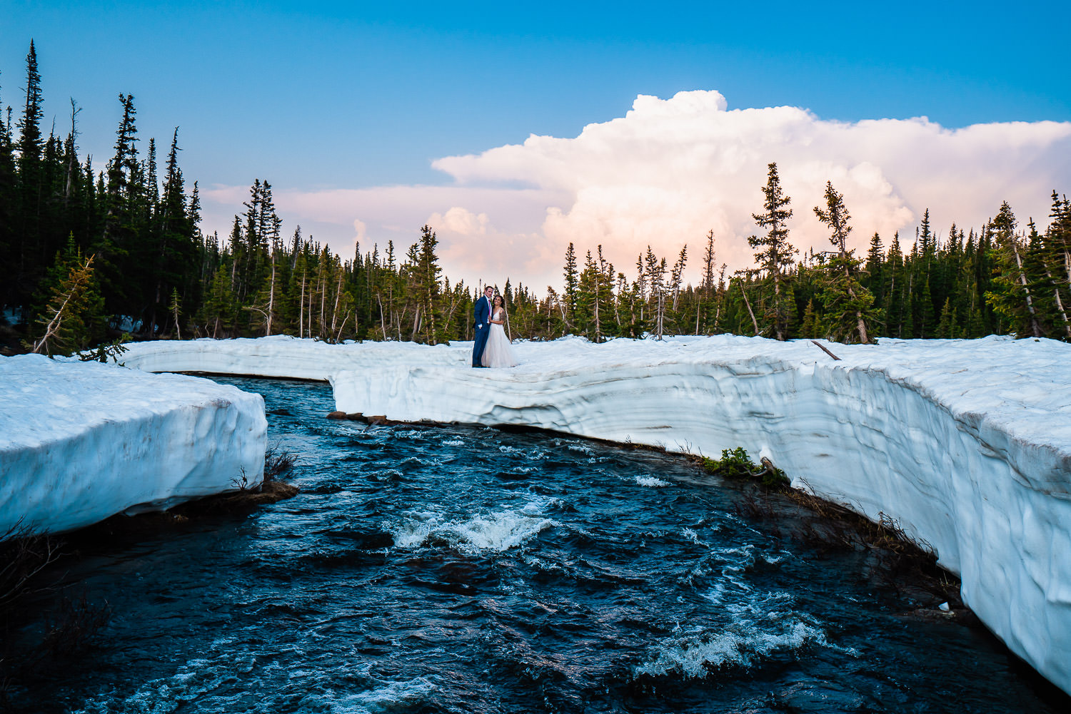 newlyweds on top of a snowy mound near a mountain stream during their Colorado winter elopement