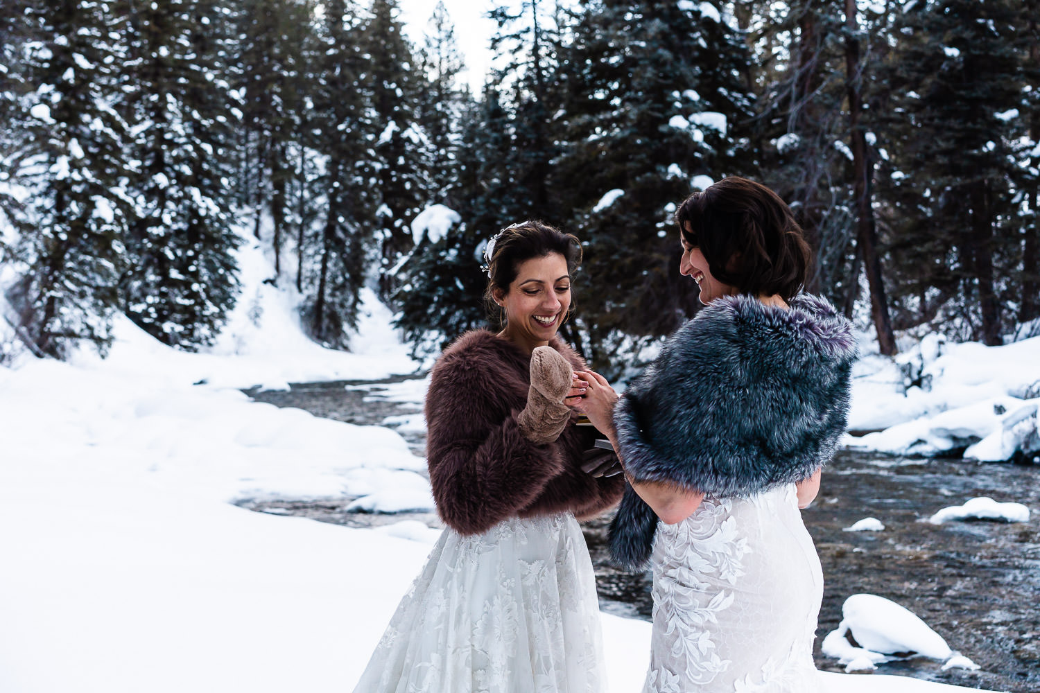 two brides exchanging rings near a snowy river during their Colorado winter elopement