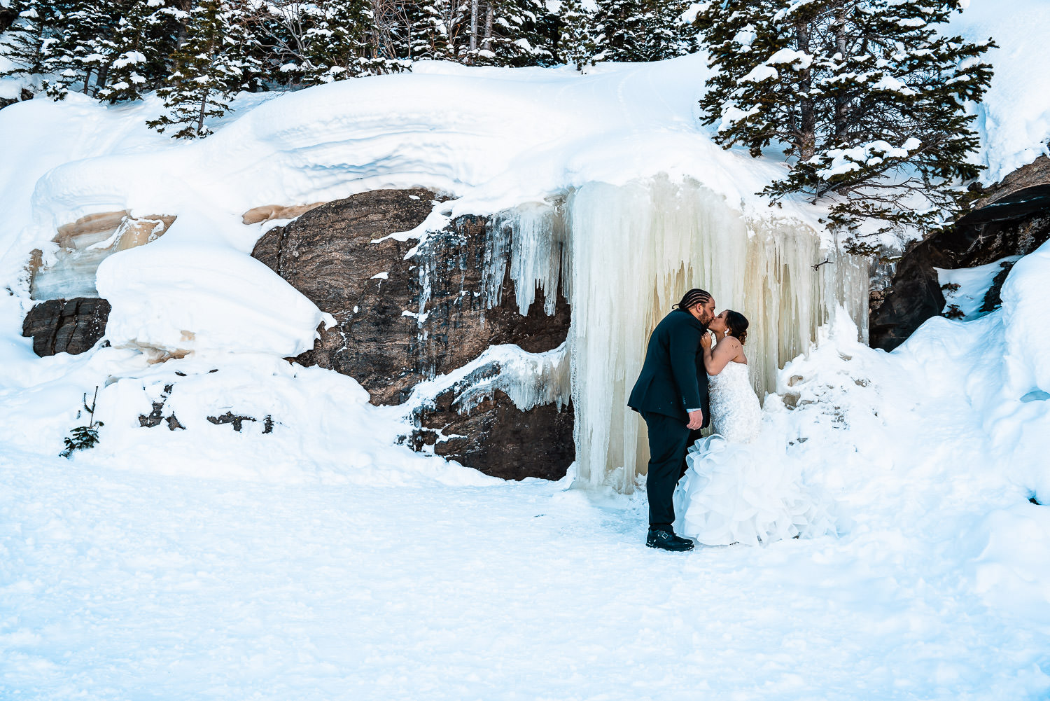 newlyweds kissing in front of a frozen waterfall during their winter elopement