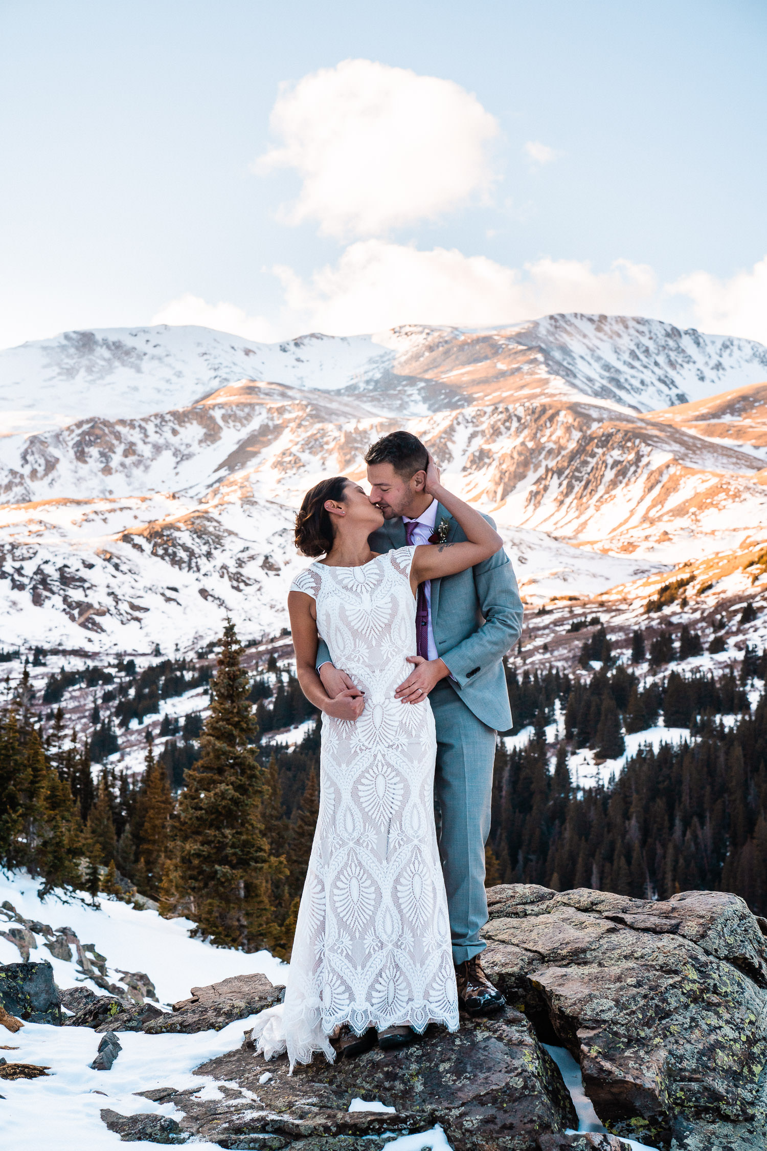 newlyweds kissing in the mountains partially covered in snow