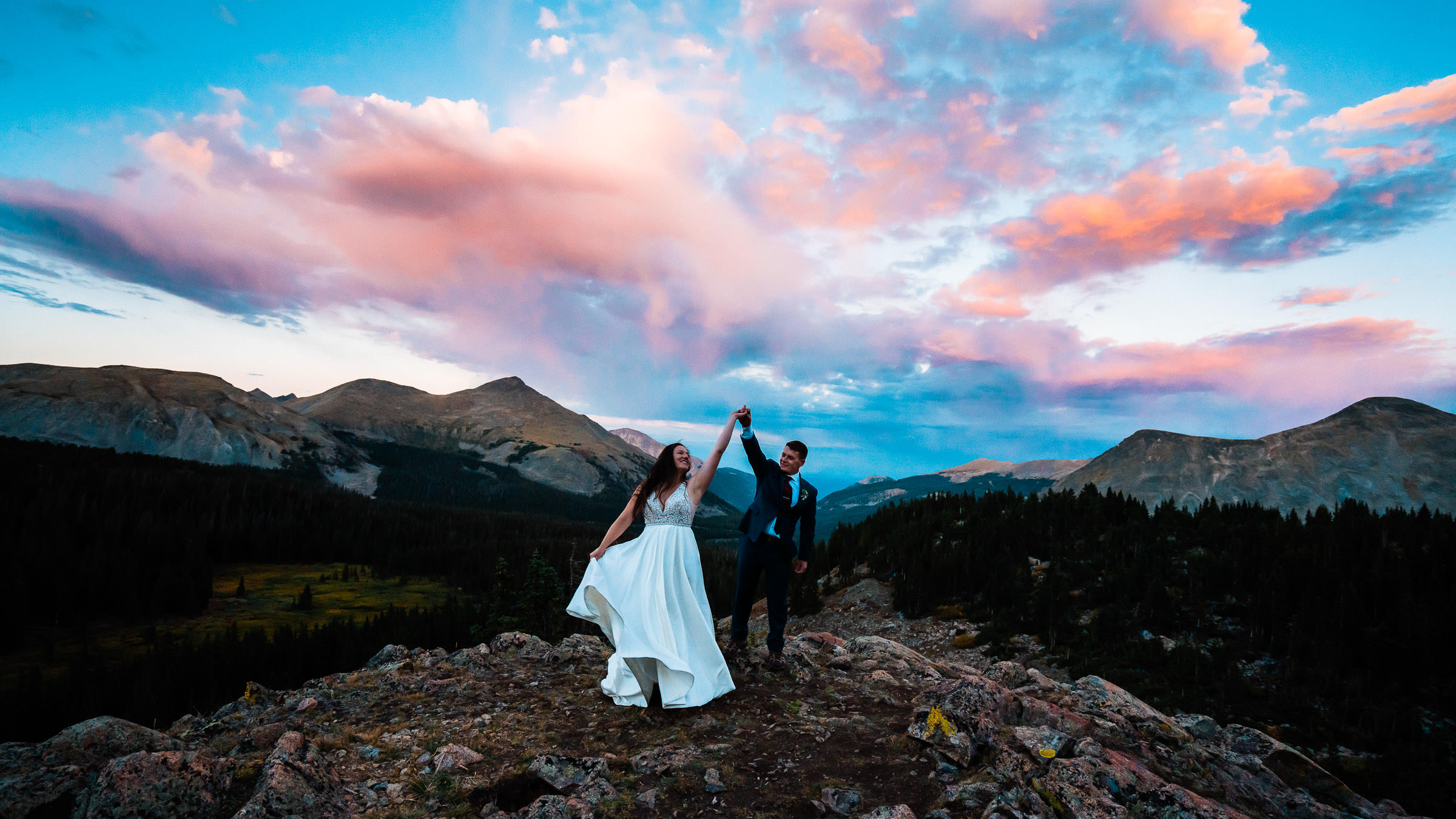 Newlyweds dance upon a mountaintop beneath an incredible pink, lavender, and crimson sunset during their Buena Vista elopement near Cottonwood Pass.