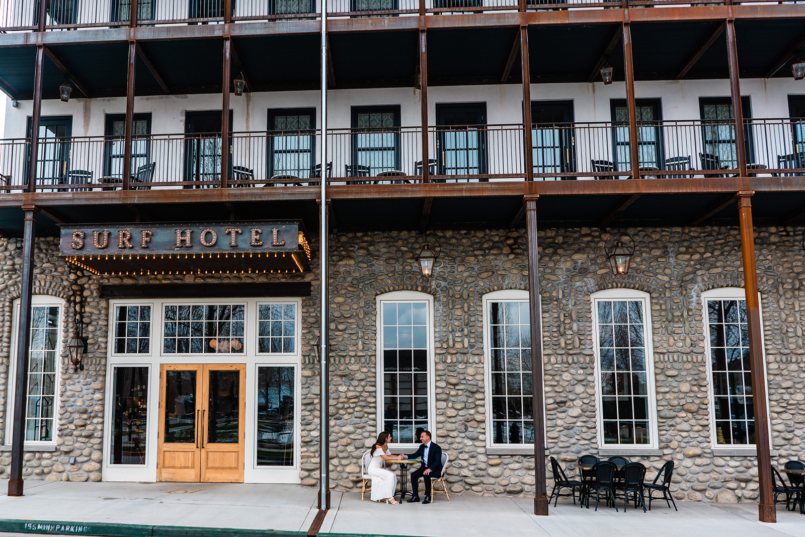 A couple sitting and chatting in front of the Surf Hotel, characterized by its grey stone facade and multiple balconies, during their Buena Vista elopement.
