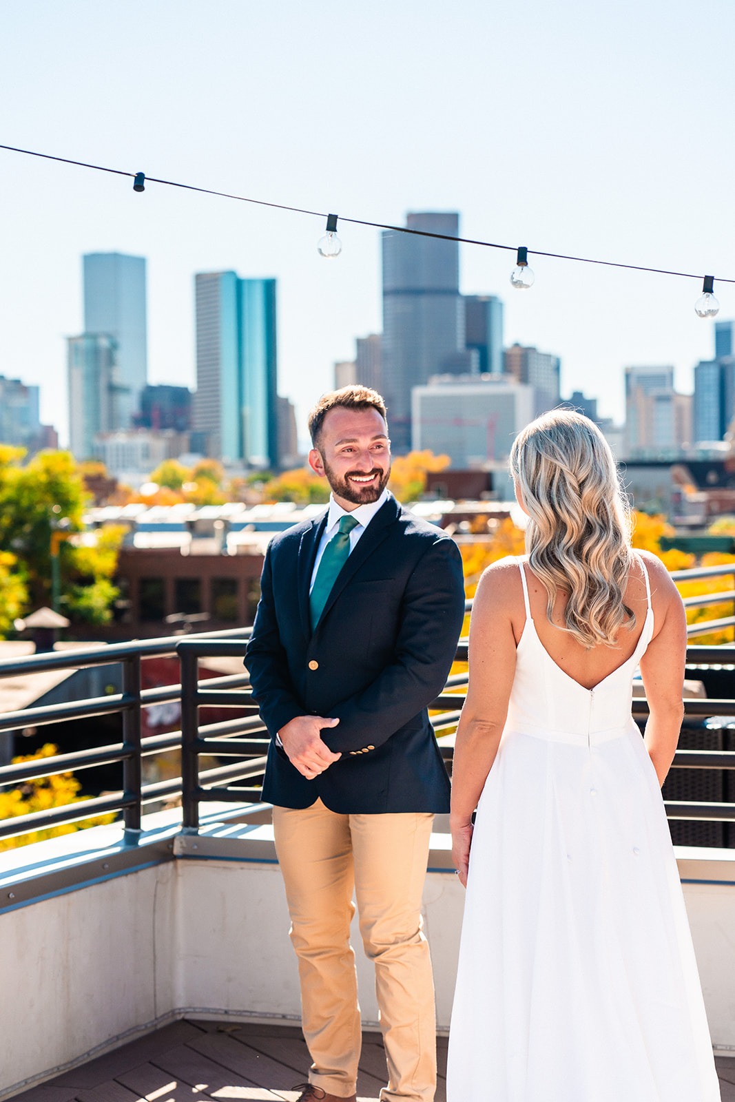A couple in wedding attire smiling at each other on a rooftop with the Denver skyline in the background during their Denver Elopement