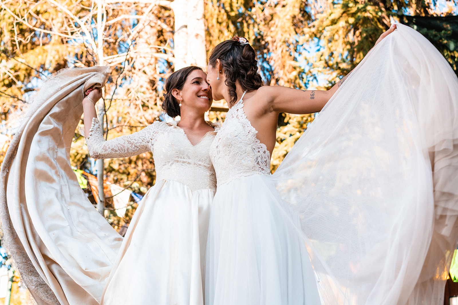 Lesbian brides smiling at one another in white elopement dresses