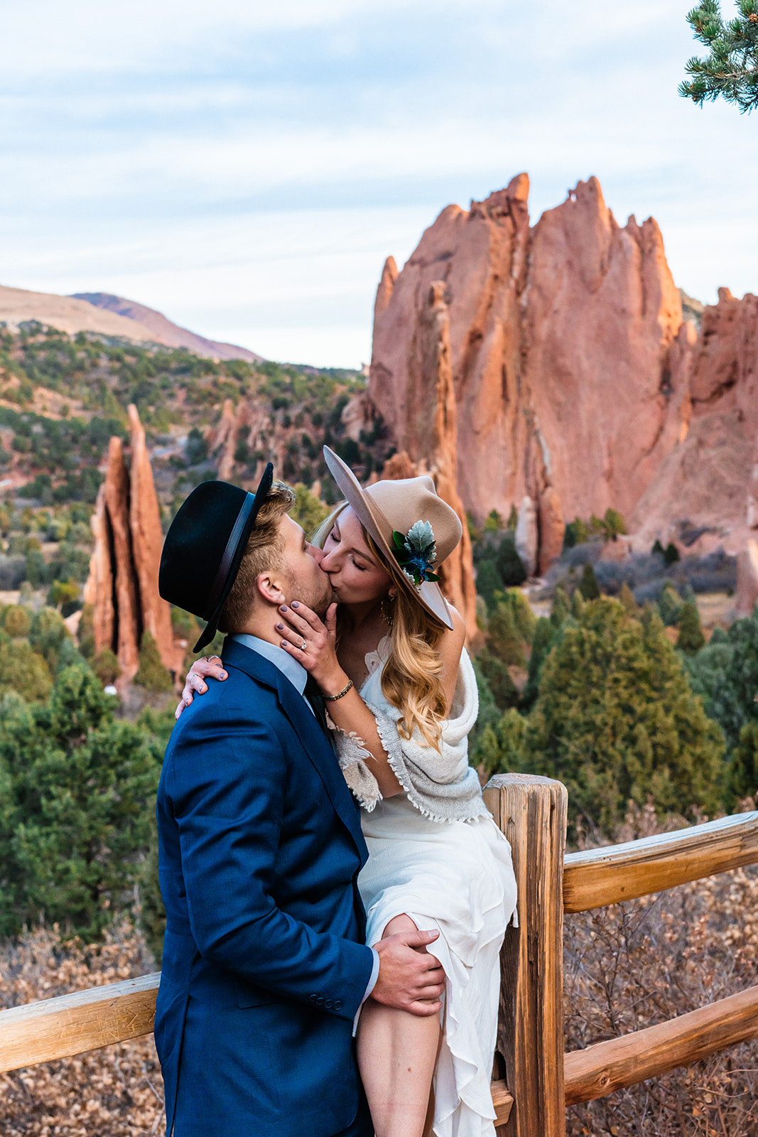 Newly engaged couple sitting in front of bright red rocks kissing at the Garden of the Gods