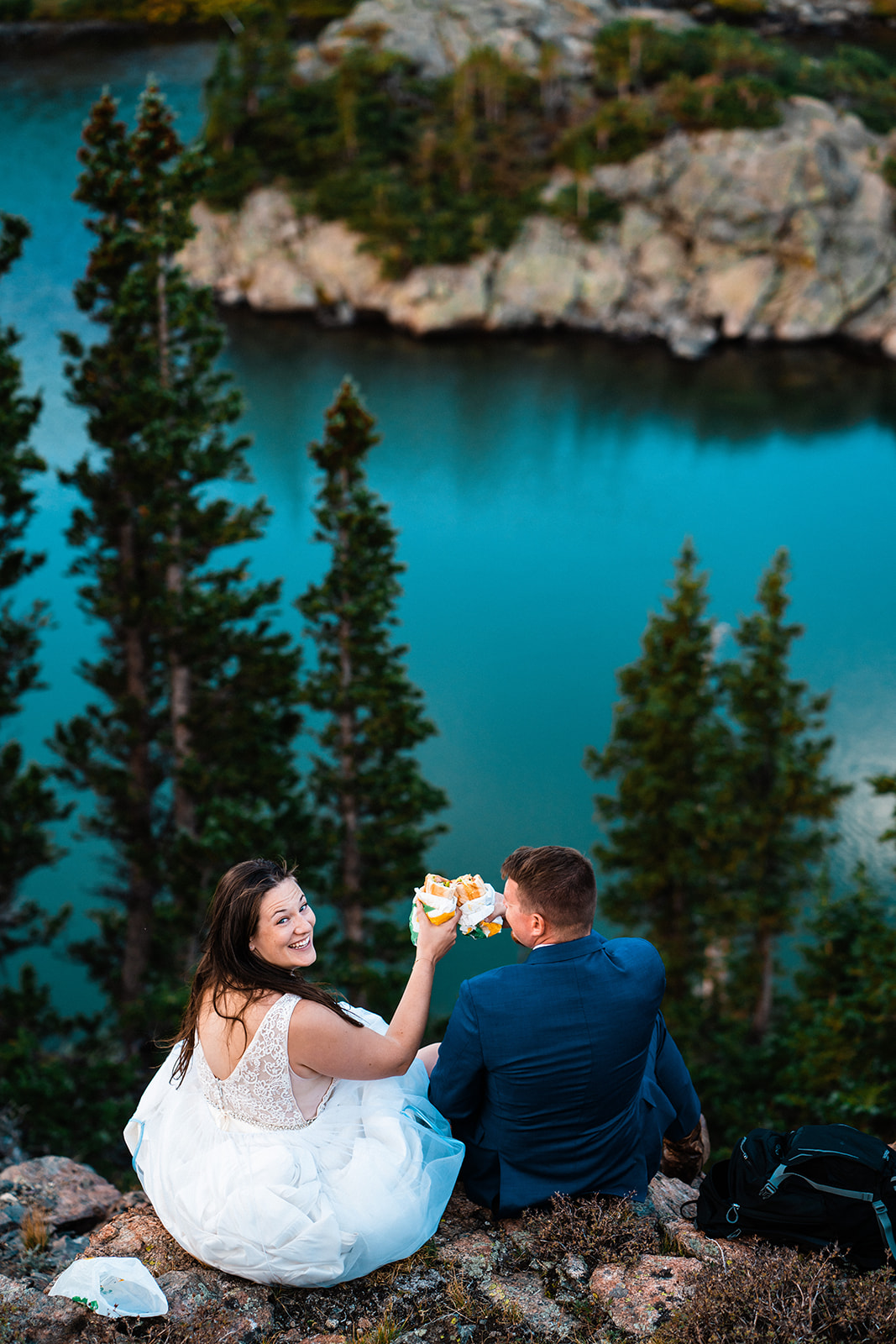 Bride and groom eating sandwiches at alpine lake