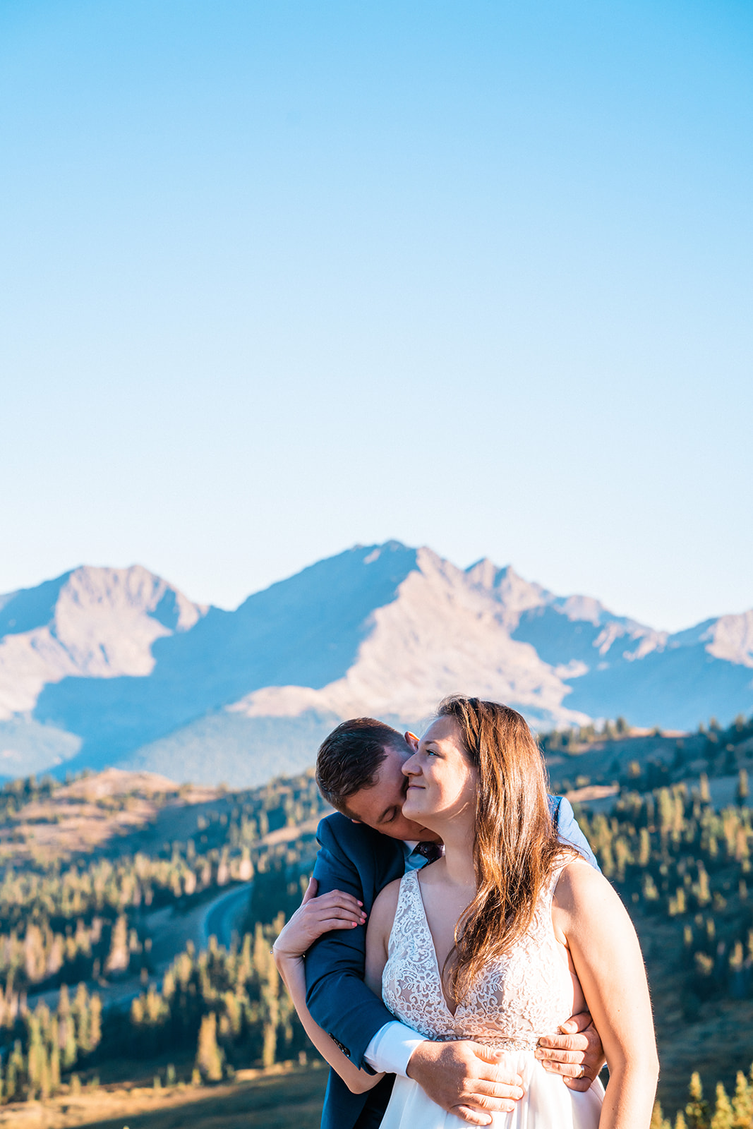 Groom kissing brides cheek with the Colorado mountains in the background