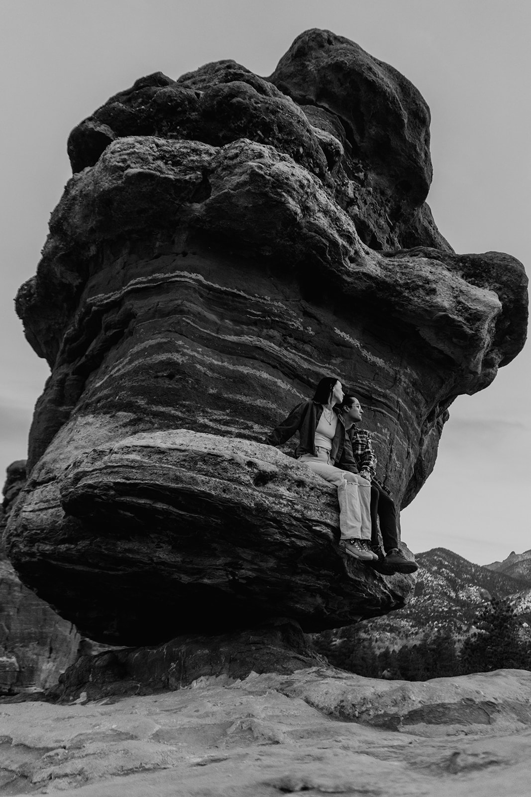 Black and white photo of newly engaged couple sitting on rock formation