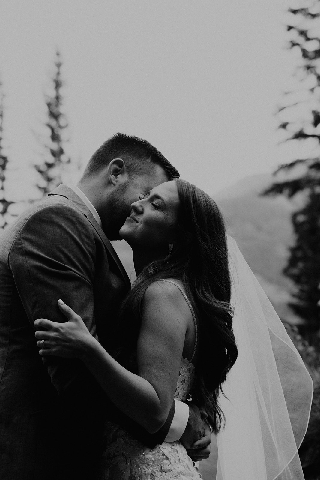 Black and white photo of groom kissing bride on the cheek