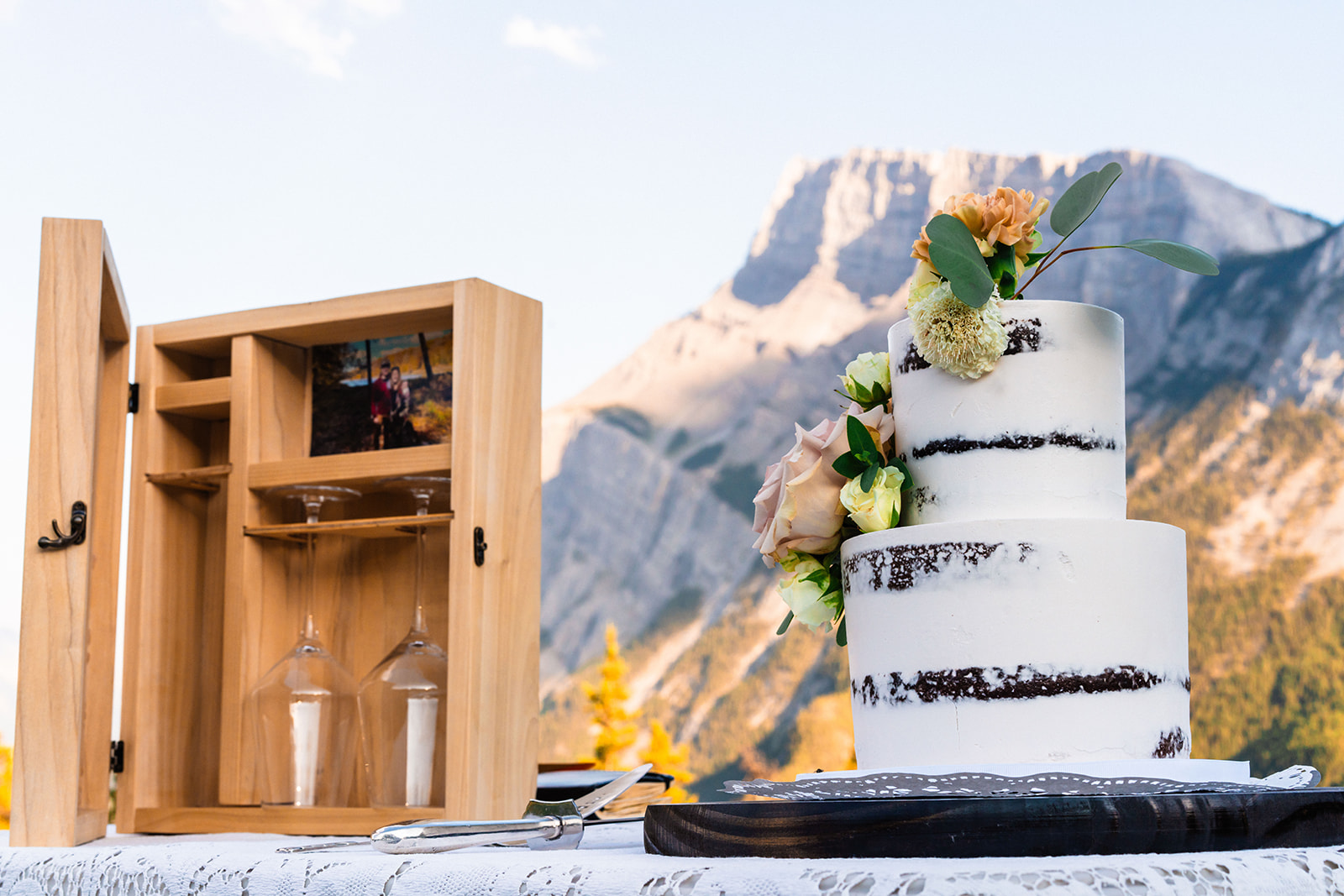 Beautiful white wedding cake next to wooden time capsule box with champagne glasses
