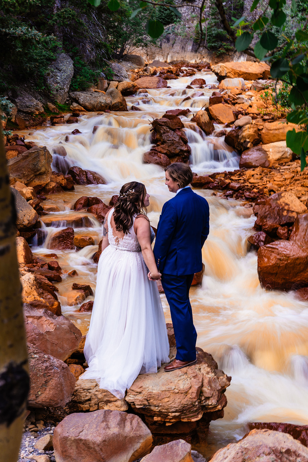 Lesbian couple looking at one another endearingly near a waterfall