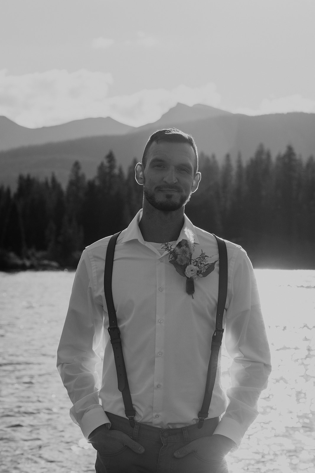 Black and white photo of Groom posing in overalls and khakis near the San Juan Mountains shoreline