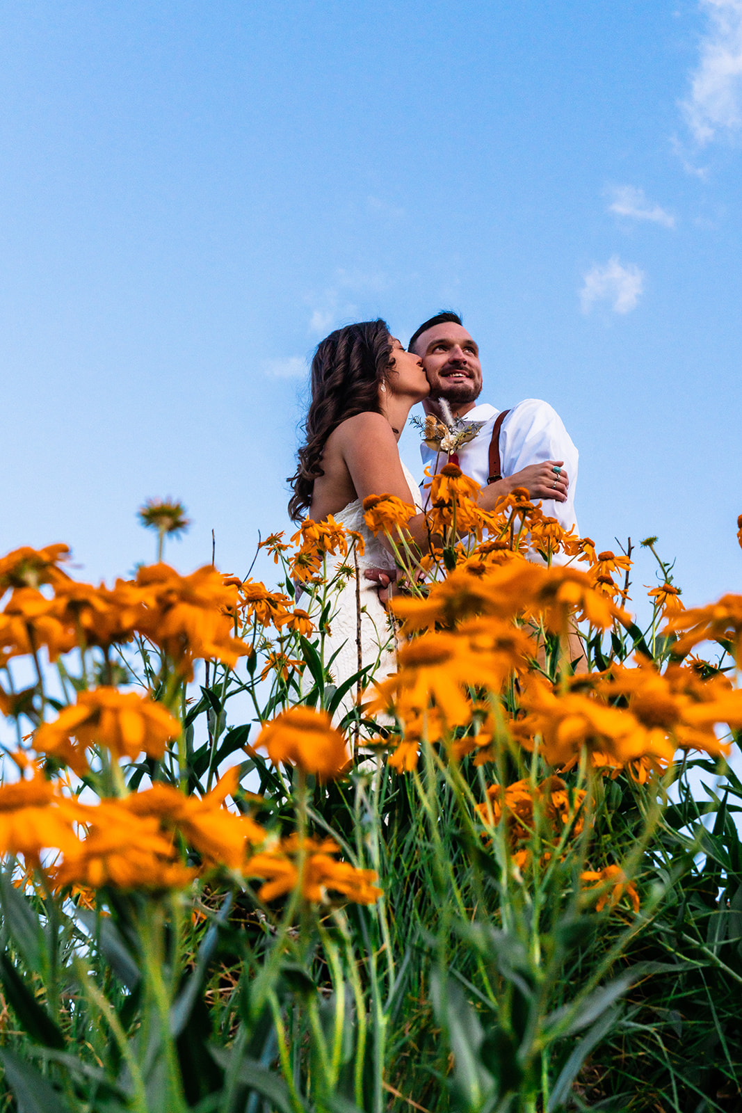 Bride kissing groom cheek standing next to beautiful orange flowers