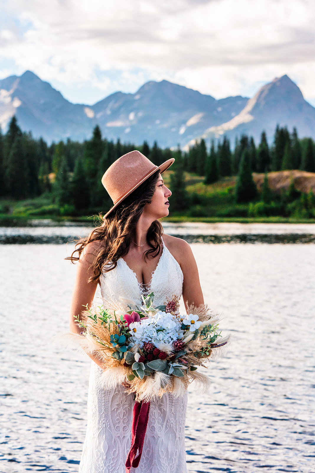 Beautiful bride in a white wedding dress posing at a shoreline in the San Juan Mountains