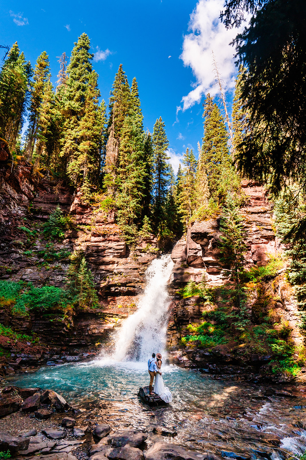 Bride and groom standing near a waterfall in the San Juan mountains