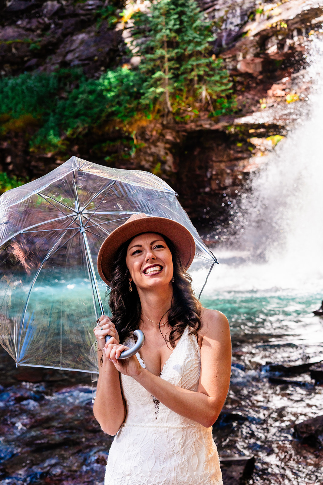 Stunning bride smiling holding an umbrella sitting near a waterfall in the San Juan Mountains