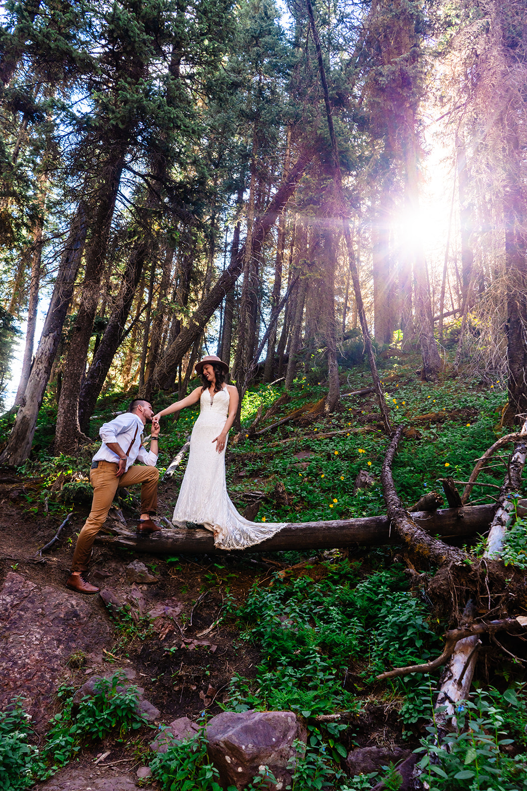 Groom kissing brides hand while she stands on a fallen tree