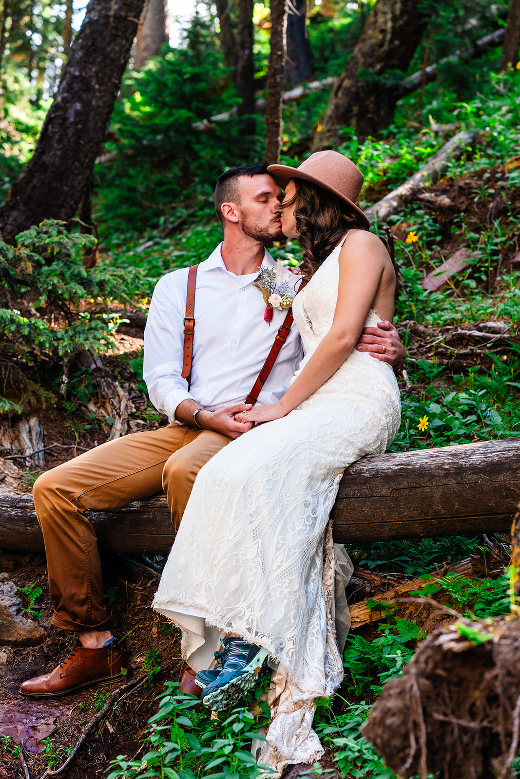 Bride and groom kissing on fallen tree in the forests of the San Juan mountains