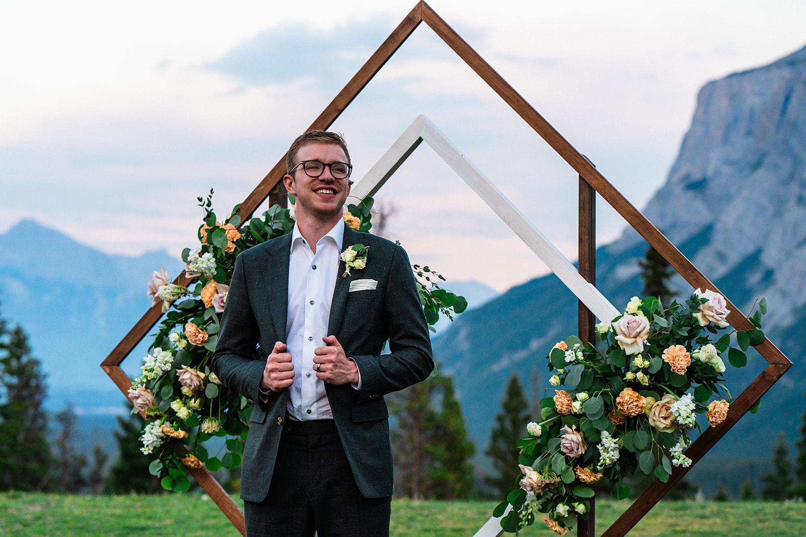 Groom posing in wedding suite in front of wooden arch