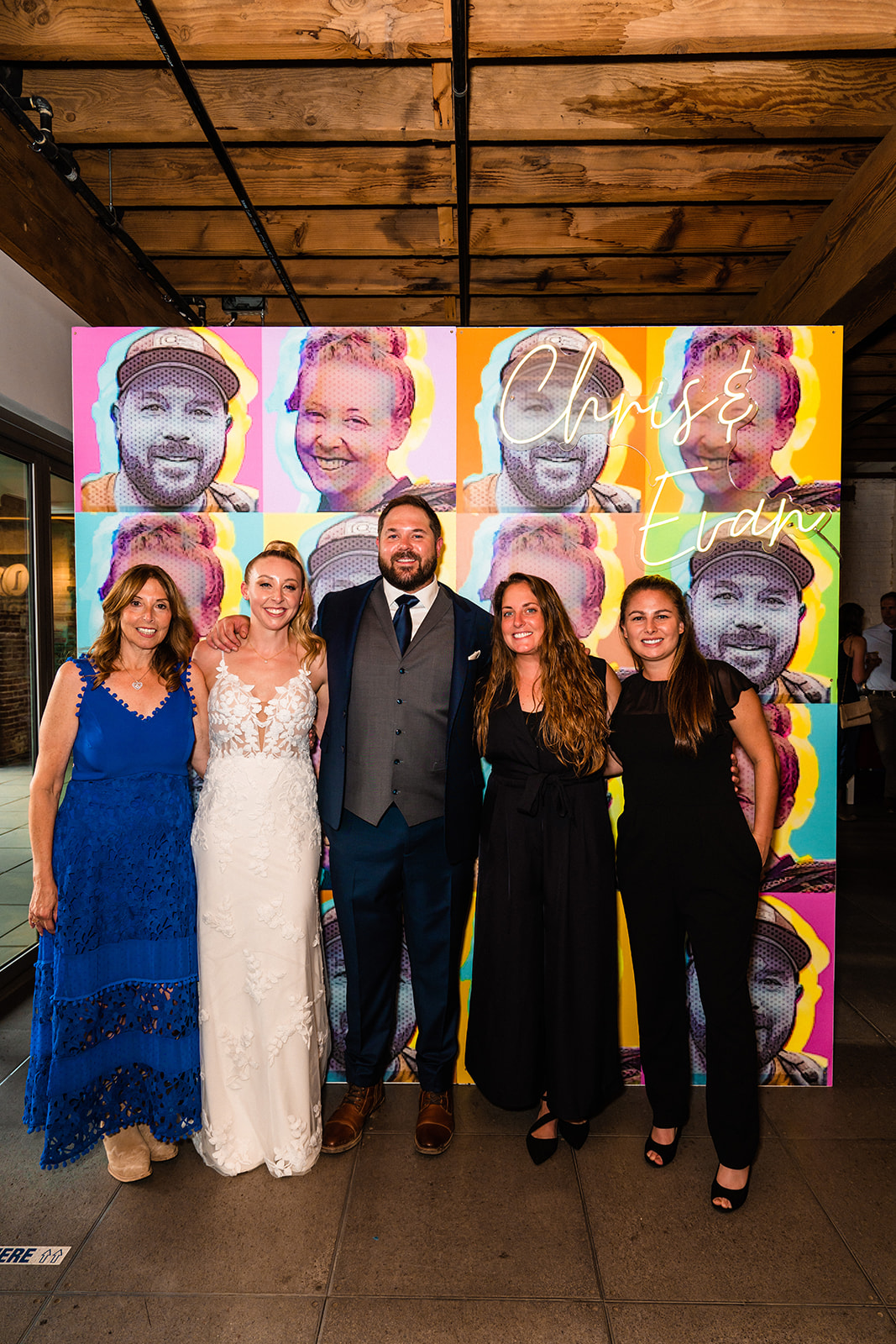 Bride and groom posing with family and friends in front of an art piece of their faces