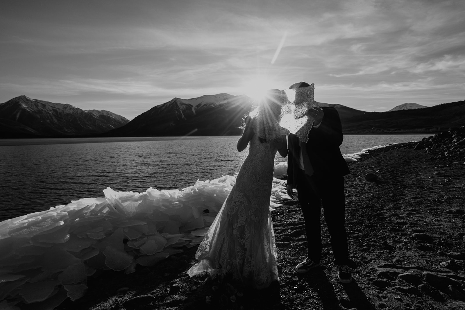 Black and white photo of Bride and groom kissing behind a piece of ice