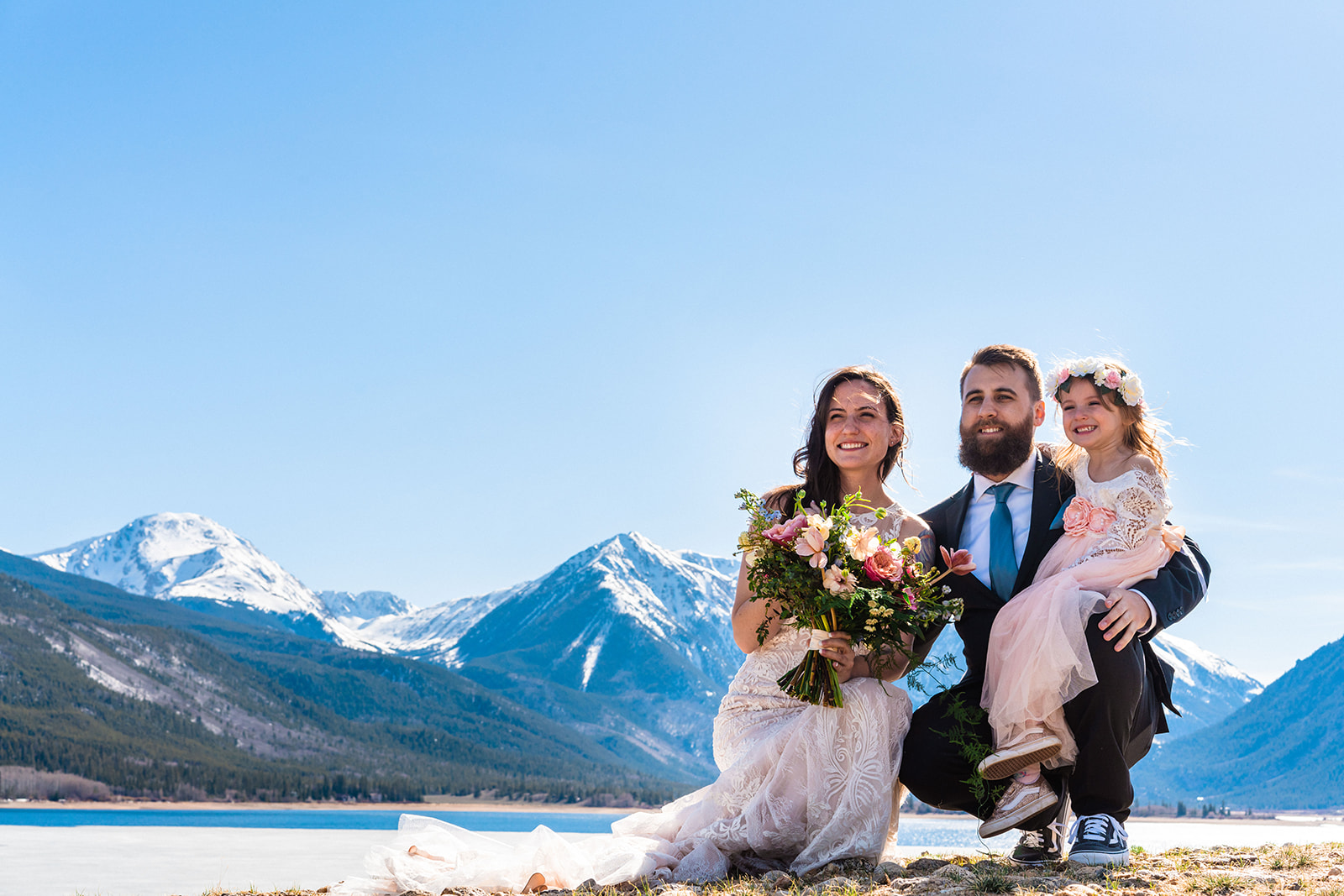 Bride, groom, and daughter smiling and posing near the Twin Lakes