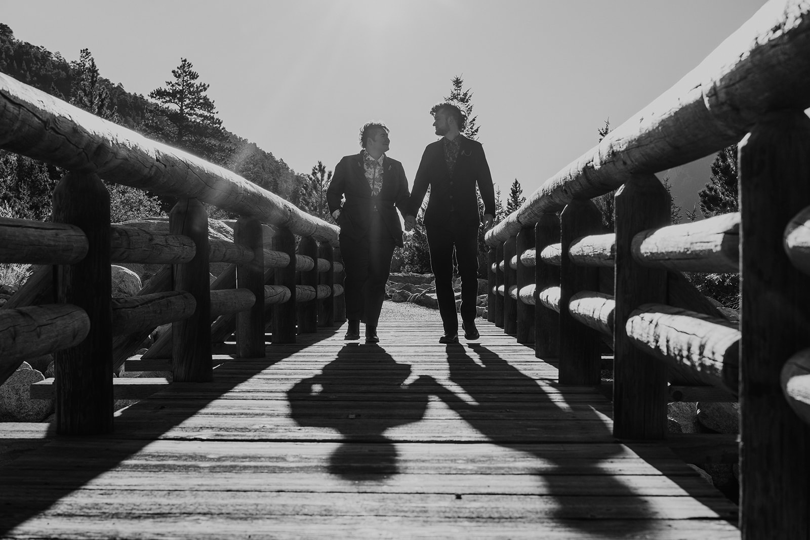 Black ad white photo of couple holding hands walking down a bridge