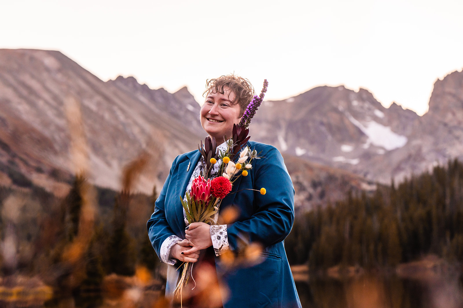 Newlywed smiling holding a bouquet in a beautiful blue tux and red pants