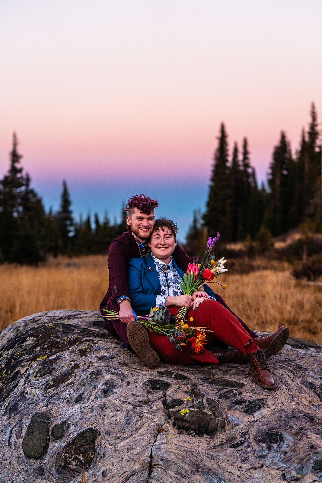 A couple embracing and sitting on a boulder with a Colorado sunset in the background
