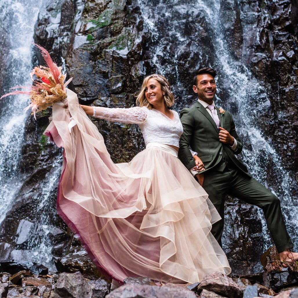 a couple holding hands in front of a waterfall on their Colorado adventure elopement