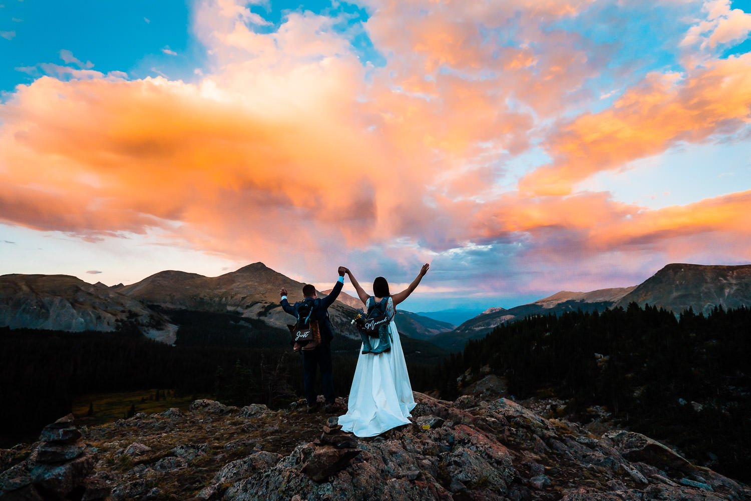 A mesmerizing elopement photoshoot captures a bride and groom standing on top of a mountain at sunset, bathed in the enchanting golden hues of dusk.