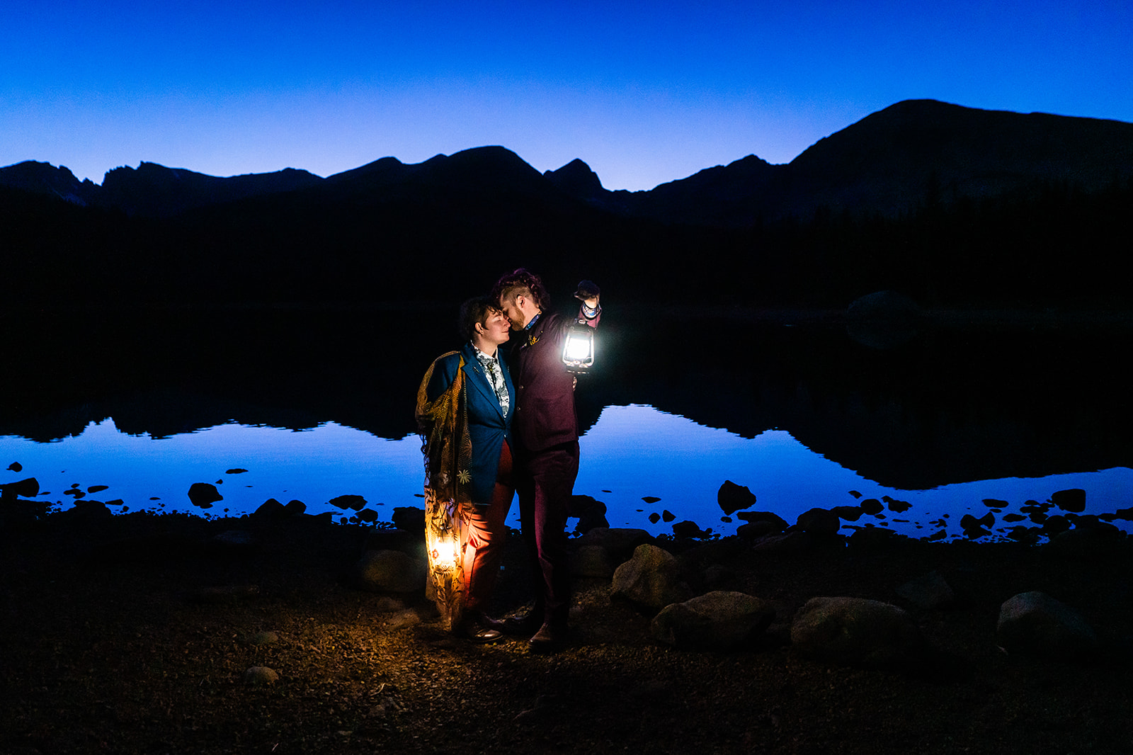 Two people holding lanterns in front of a lake at night.