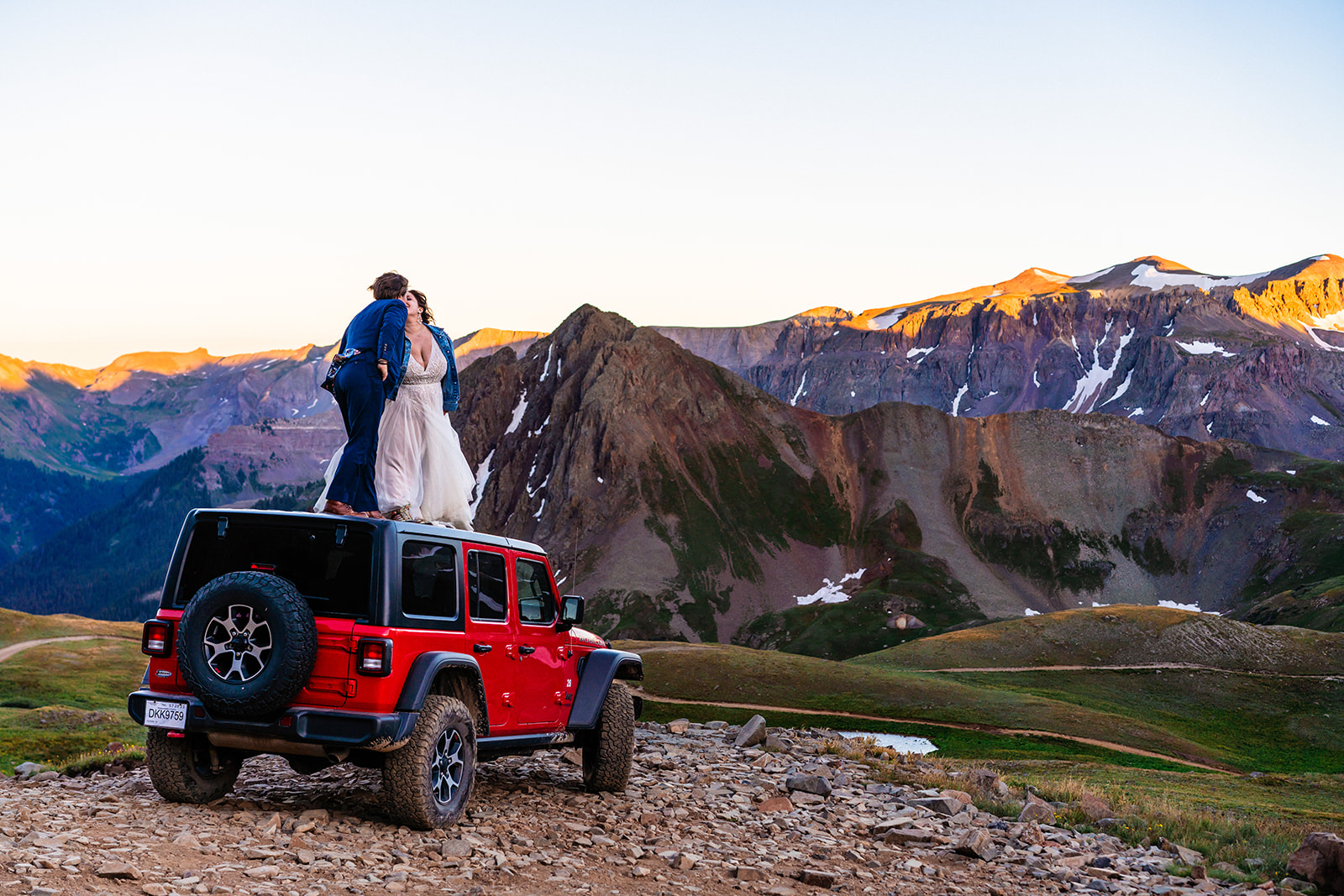 A bride and groom standing on top of a jeep in the Telluride mountains.