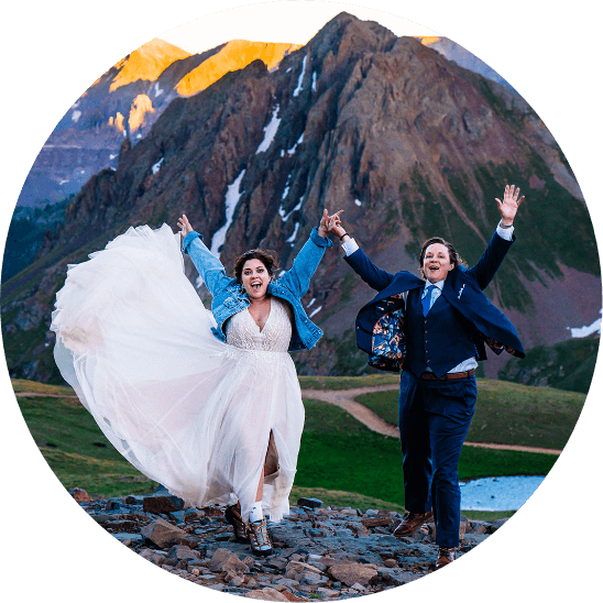 A couple holding hands and throwing their arms in the air as they celebrate their elopement in the Colorado mountains